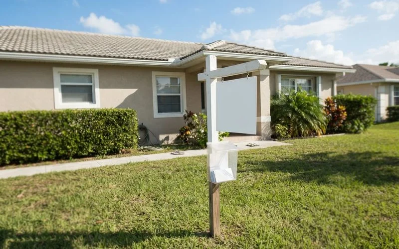 A "for sale" sign in front of a house with a moving truck in the driveway